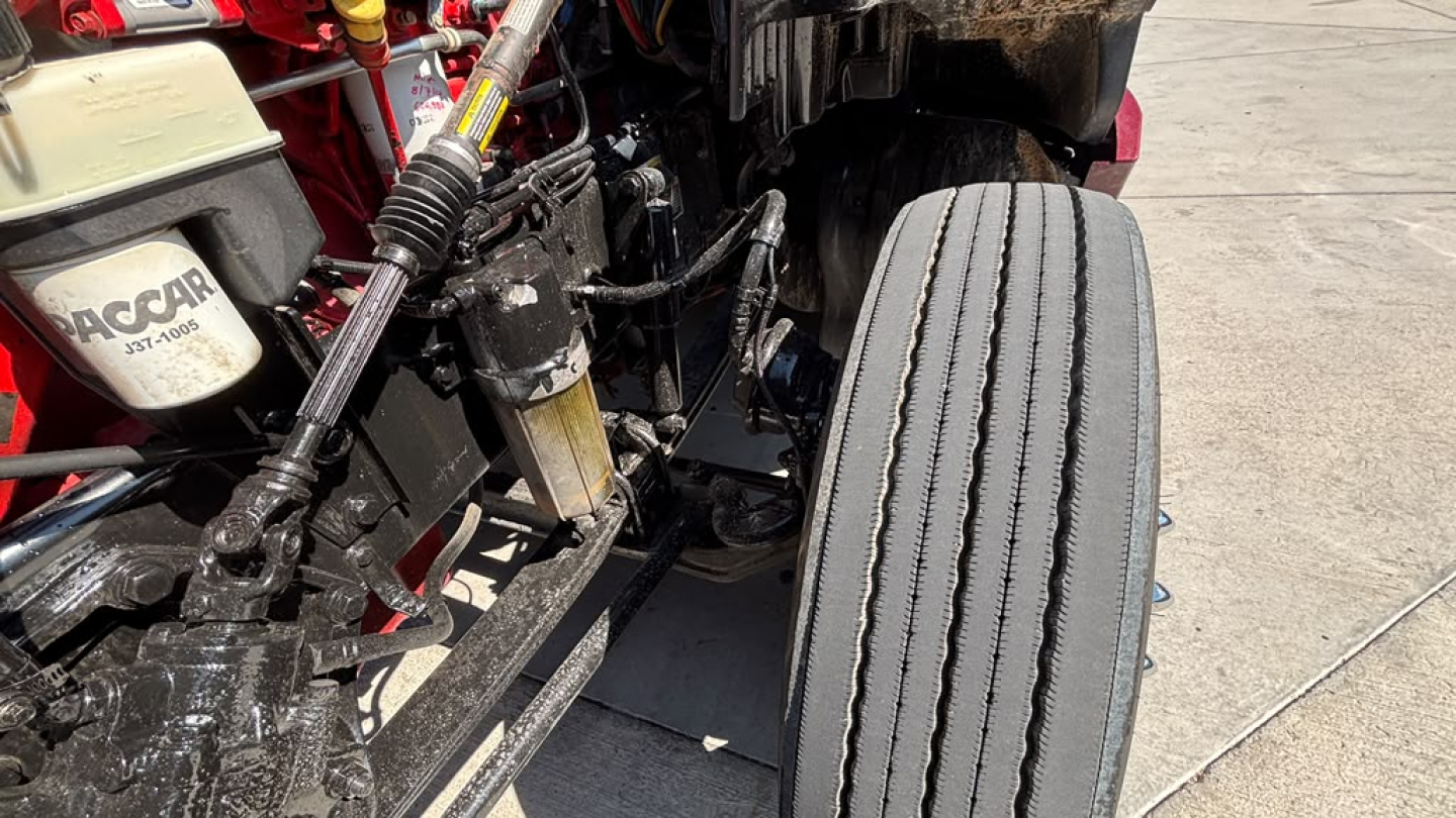 Kenworth T680 chassis view showing front suspension, steering linkage, and large front tire with dual tread grooves.