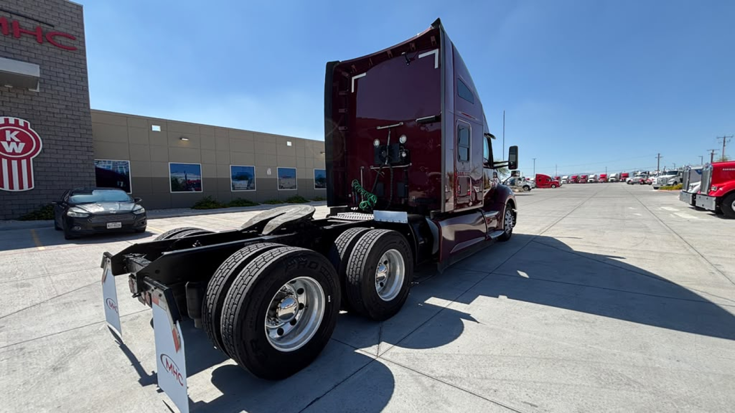 Kenworth T680 tractor in-service view from rear-left showing tandem axles and chassis, no trailer attached, with dealership building in background.