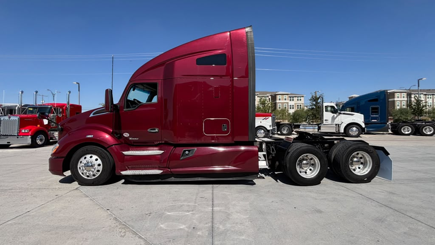 Kenworth T680 side view cab with red paint and sleeper, showing chassis and rear axles.