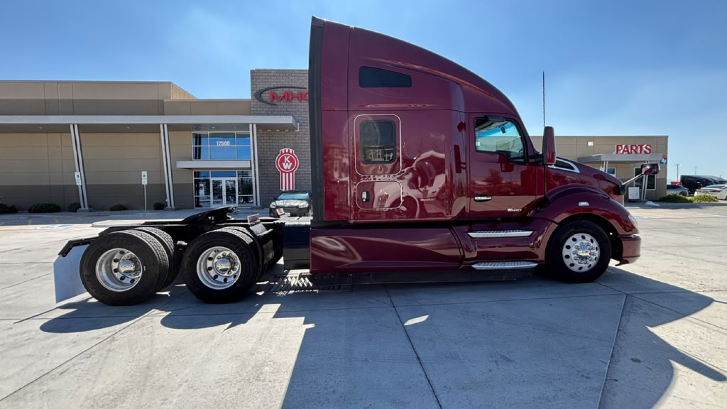 Kenworth T680 tractor cab side view showing maroon color and dual rear axles with chrome wheels.
