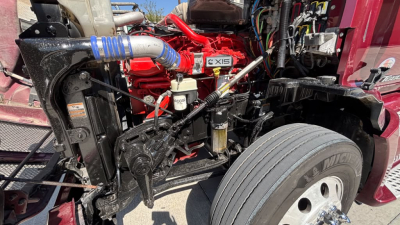 Kenworth T680 engine bay showing red engine with X15 badge and surrounding hoses and components.