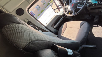 Cab interior of a Kenworth T680 showing driver's seat and steering wheel with fabric upholstery and dashboard controls.