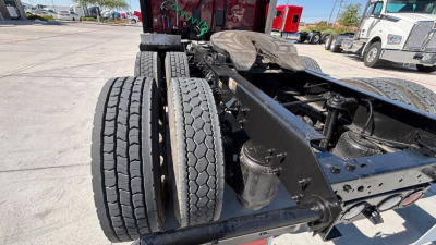 Dual rear wheels and chassis of a Kenworth truck showing a fuel tank, suspension, and frame with an elevated cab area in background.