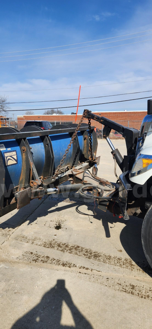 Truck hitch and equipment on a dump truck attachment, visible chain, hook, and hydraulic linkage components.