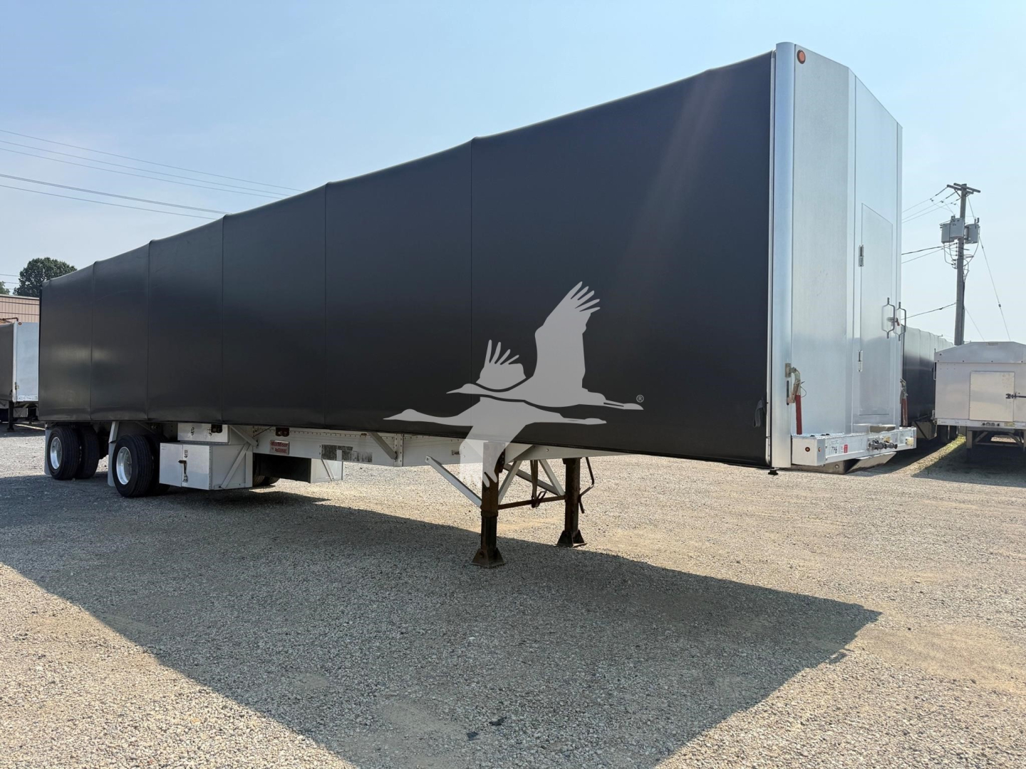 Truck trailer showing black curtain side with white logo birds form on the side and rear dual axles under, front landing gear visible.