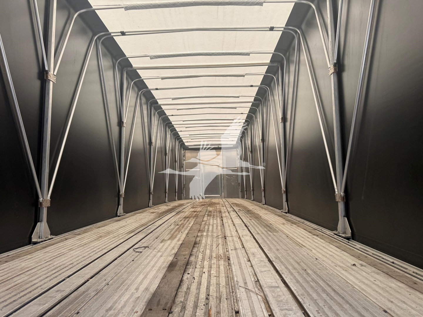 Trailer interior showing metal side rails of a curtain sider without cargo, long perspective down the empty bed.