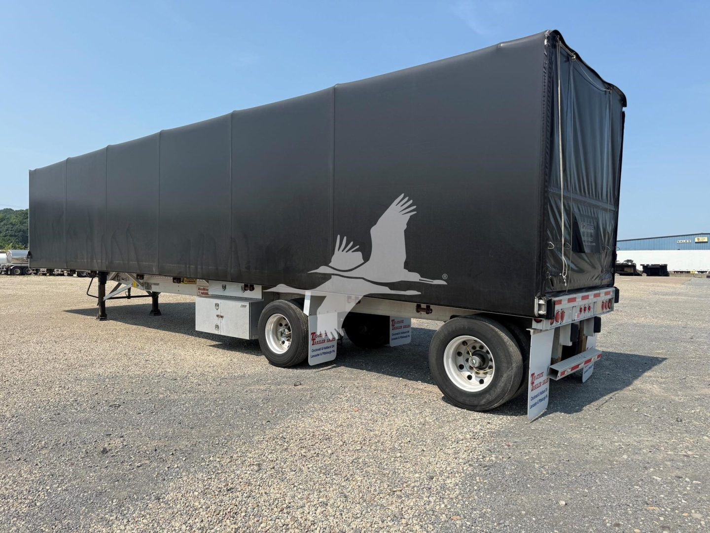 Trailer side view of a 2012 Reitnouer Maxmiser curtainside trailer with black tarp, white eagle graphic, rear underride guards, and silver wheels.