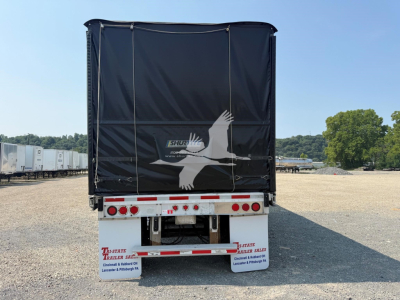 Rear view of a 2012 Reitnouer Maxmiser curtainside trailer showing tail lights, bumper, and black tarpaulin with a white bird logo.