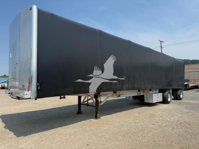 Trailer side view showing a 2012 Reitnouer Maxmiser curtainside trailer with black tarp, front-right dual wheels, and a white aerial bird logo. VIN 1RNF48A2XCR025613.