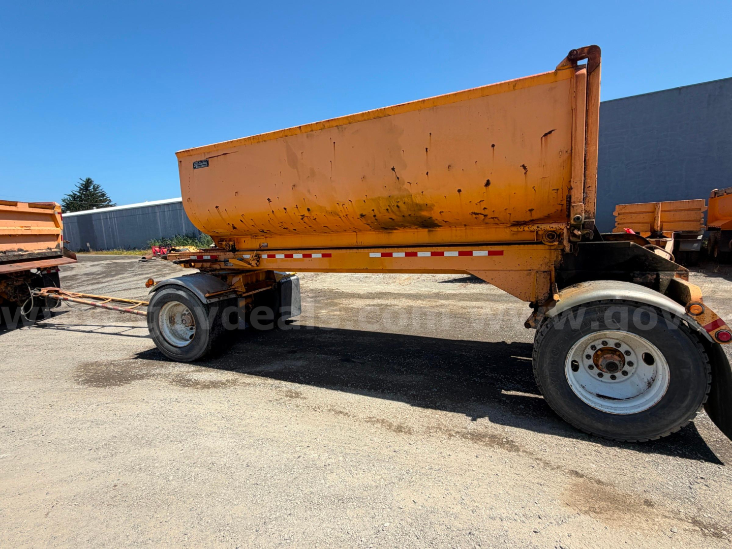 Peterbilt 378 dump trailer in-field showing orange dump body and white wheels with dual rear axle.