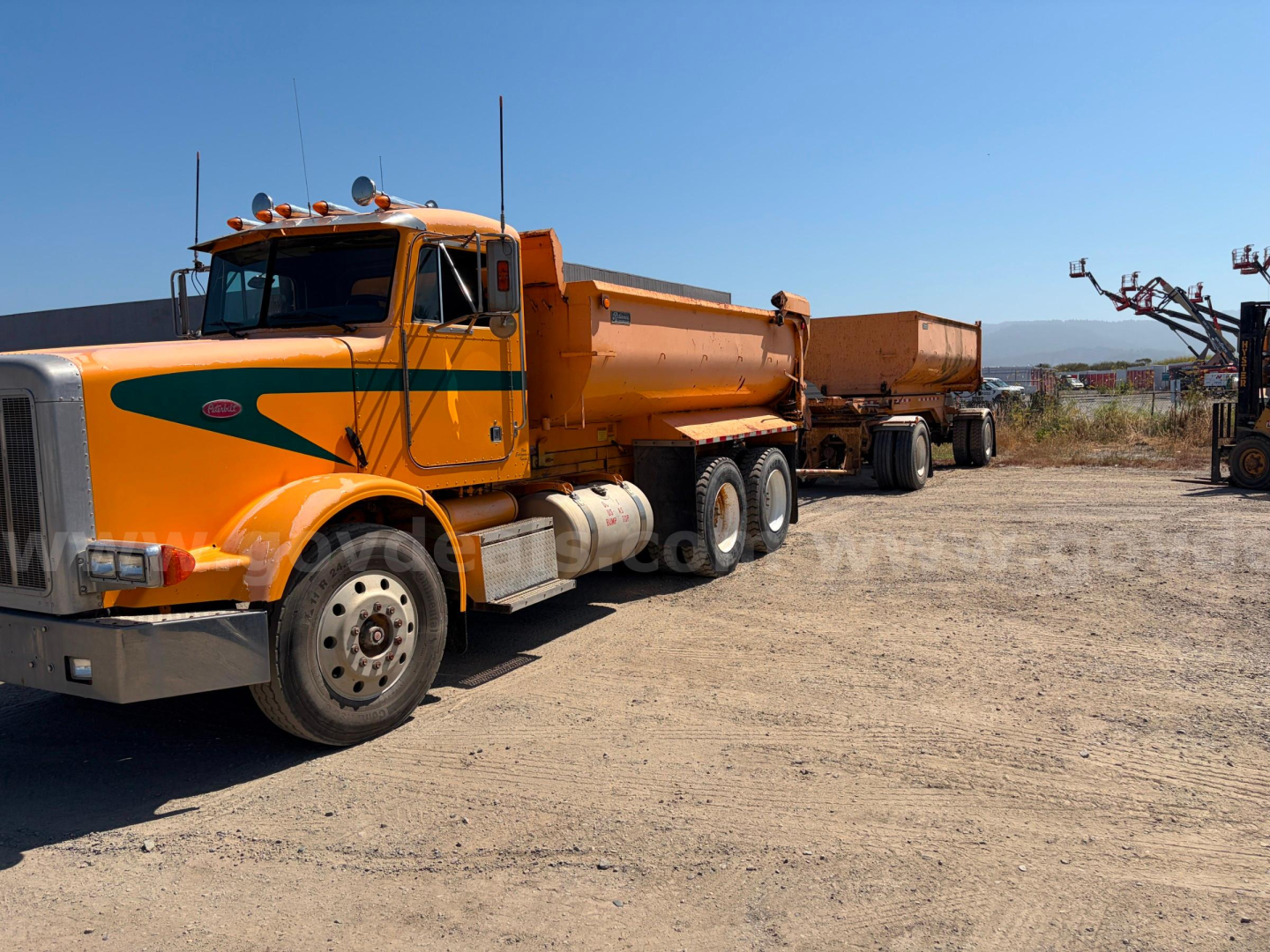 Peterbilt 378 dump truck in service showing front cab and long hopper with attached trailer in a dusty lot.