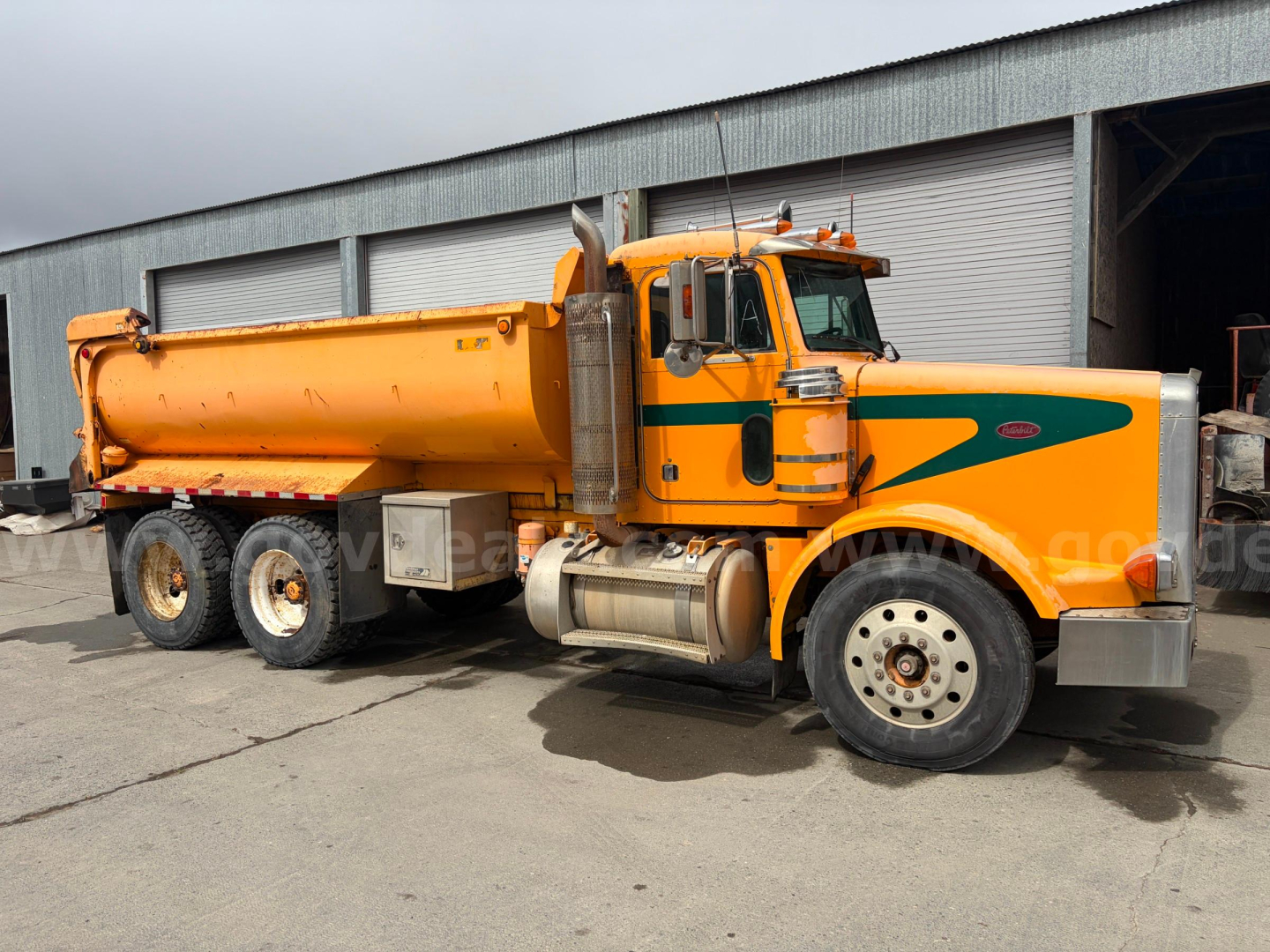 Peterbilt 378 dump truck side profile showing bright orange body with green stripe, large fuel tanks and dual rear axles.