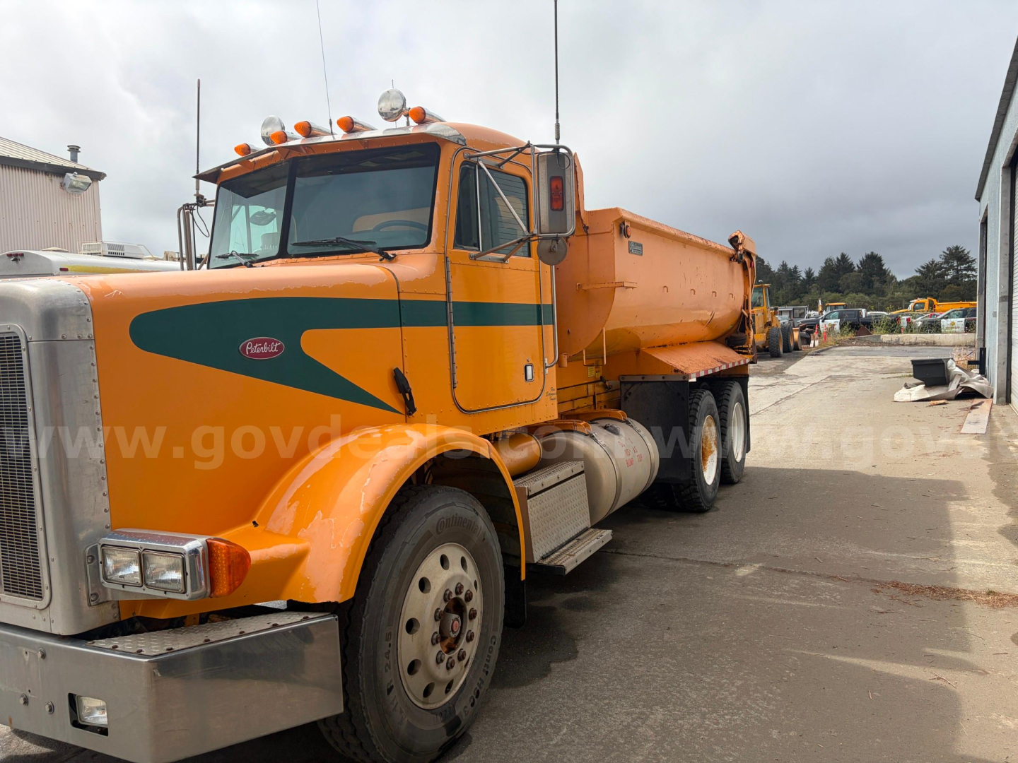 Peterbilt 378 dump truck in-service showing orange body with green decals and front chrome bumper, side view with dump bed
