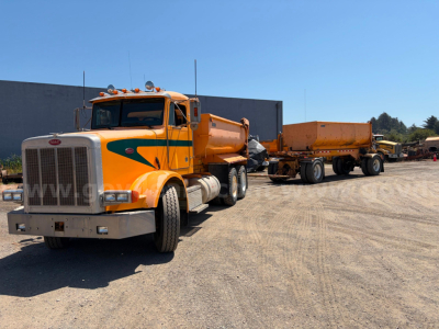 Peterbilt 378 dump truck in orange with yellow/green stripe and empty dump bed on trailer, front view in a gravel lot.