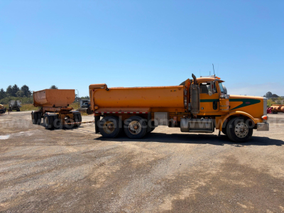 Peterbilt 378 dump truck tractor with orange cab and matching dump trailer connected, side view, clear sky and gravel lot.