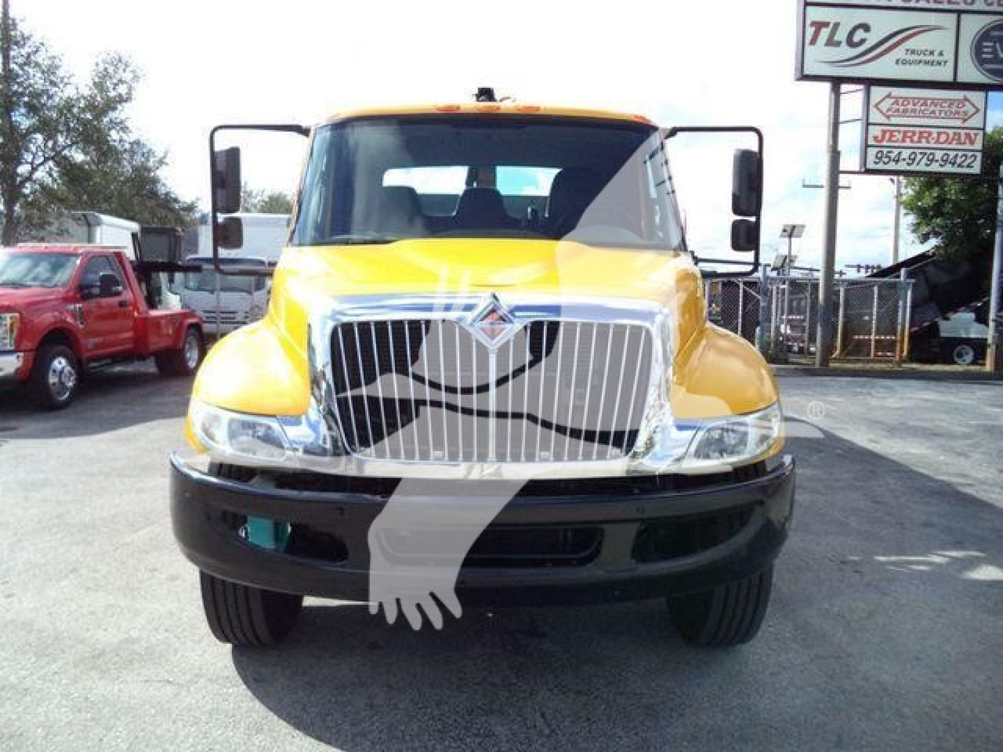 Front view of a yellow 2019 International Durastar 4300 medium-duty truck with a large chrome grille, black bumper, and side mirrors; dealership lot in background.