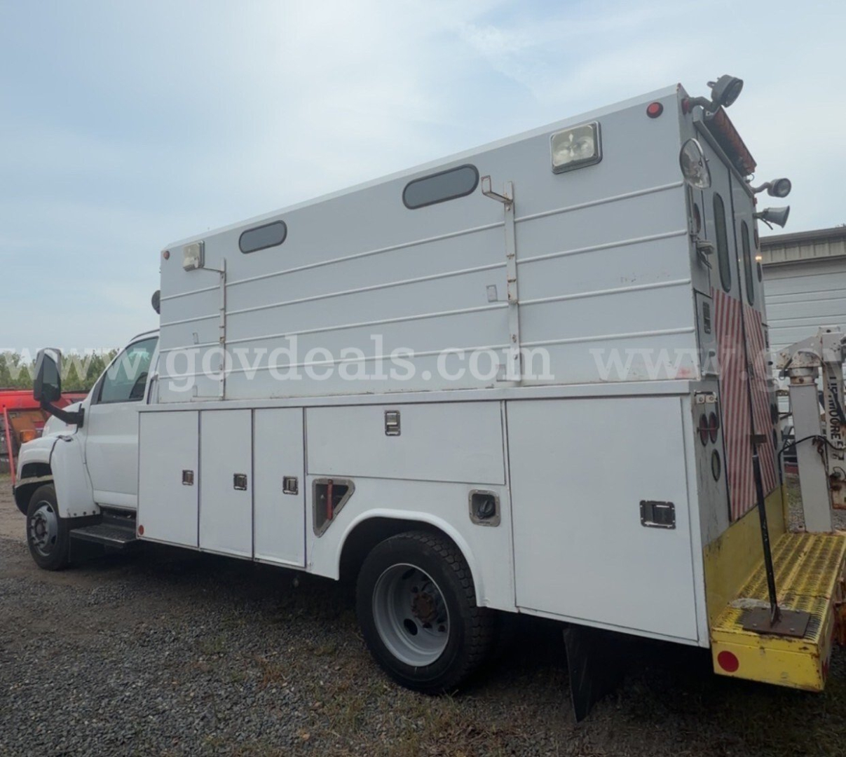 GMC utility/service truck rear-side view showing multiple storage compartments and a raised cab, silver body with yellow rear bumper step.