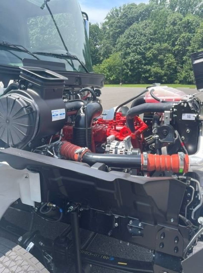 Engine bay of a 2027 Hino L6 box van showing red engine components, hoses, and air intake, with surrounding chassis and hood structure visible.