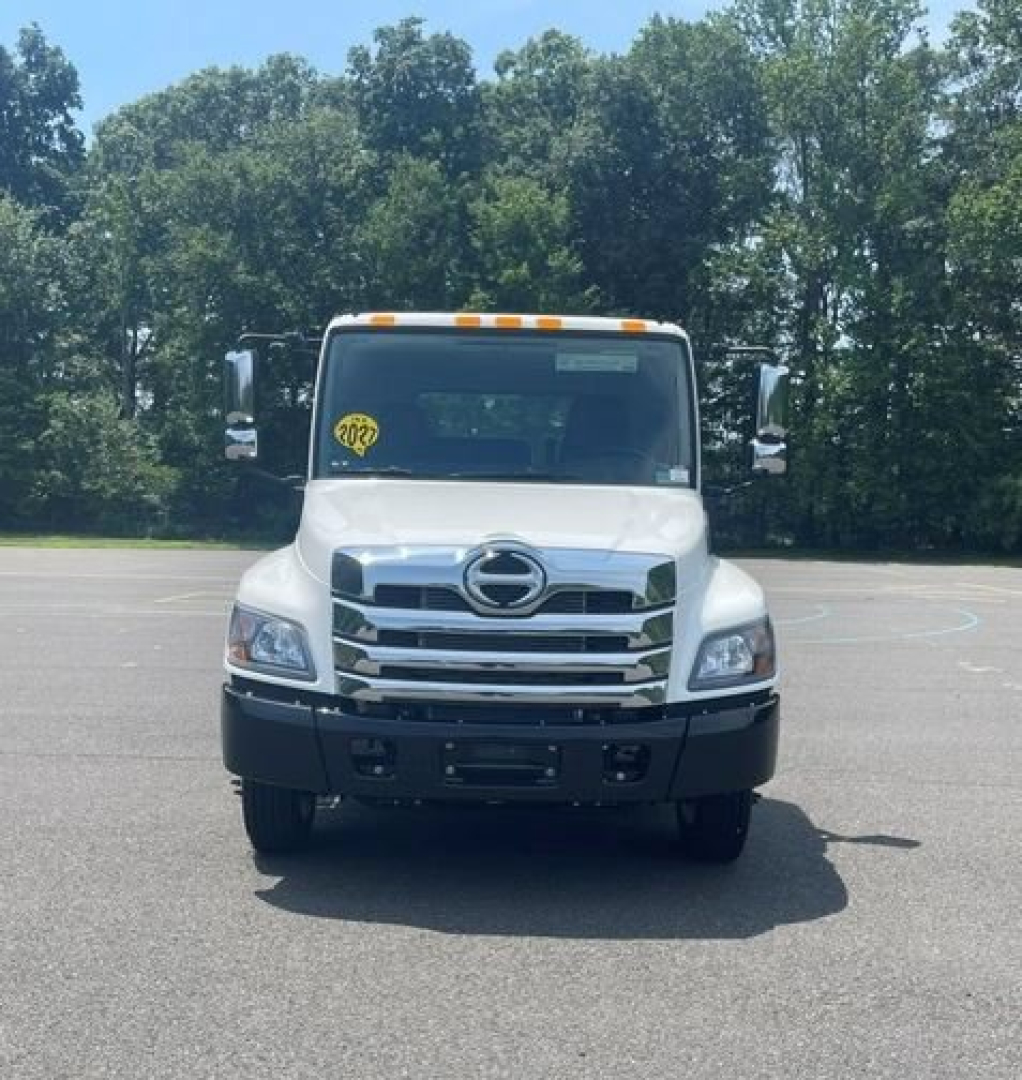 Front view of a white Hino box truck with large grille and Hino emblem, stock number badge on windshield, in a parking lot.