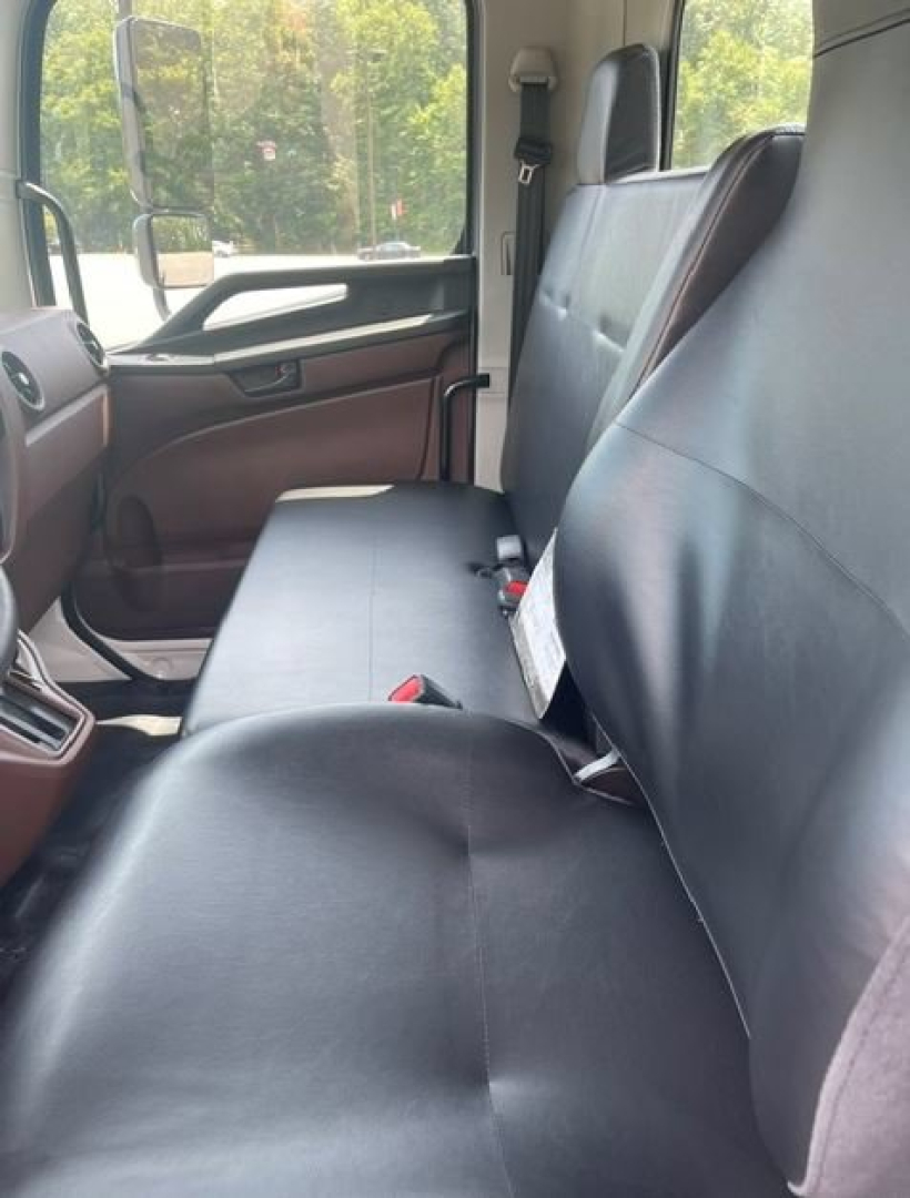 Vehicle interior showing front bench seat with dark upholstery, dashboard on left, doorway and window visible.