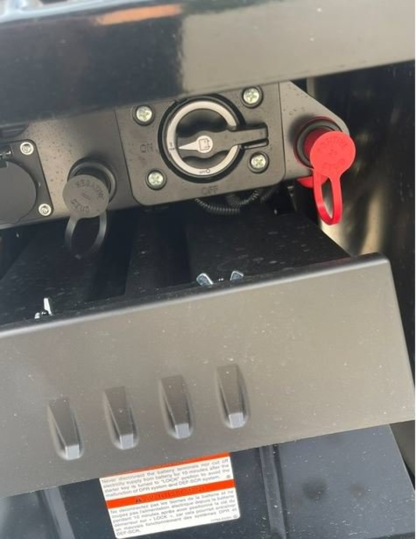 Truck fuel cap and hitch area with red locking pin and circular fill cap visible on a black panel.