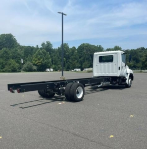 Box van truck chassis with cab and long wheelbase frame, side view showing empty flatbed chassis and single rear axle on a paved lot.