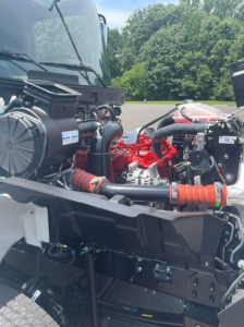 Engine bay of a 2027 Hino L6 box van showing red engine components, hoses, and air intake, with surrounding chassis and hood structure visible.