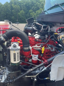 Truck engine bay with red engine block, hoses, and filters visible; includes white Racor fuel filter canister and other engine components.