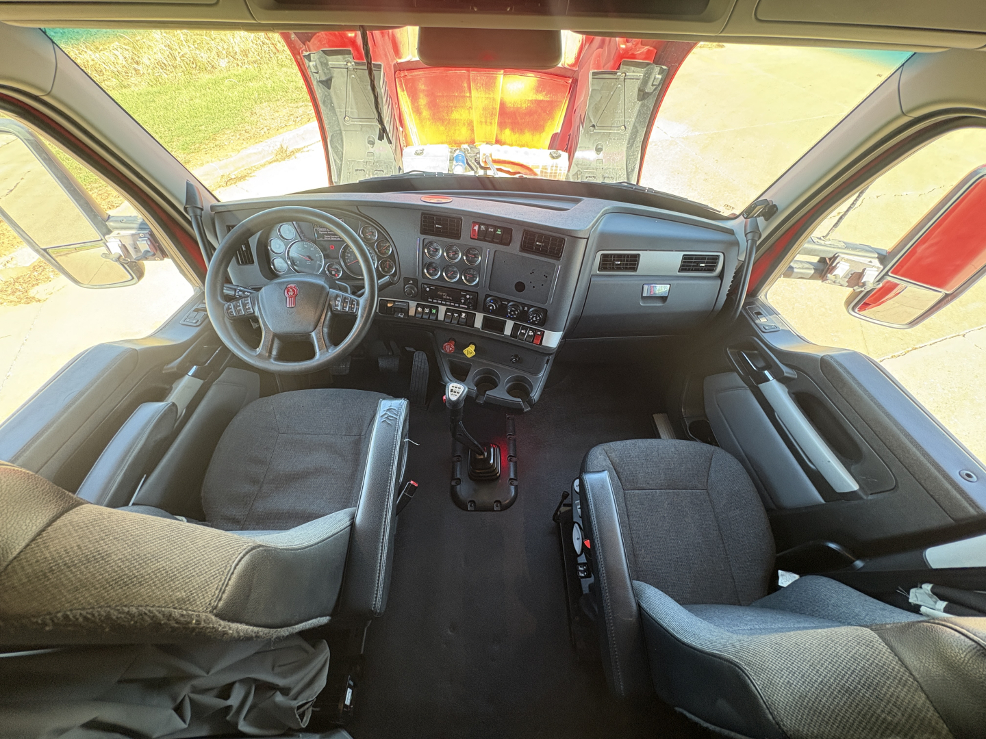 Kenworth T680 truck interior showing steering wheel, dashboard with gauges, front seats, and center console viewed from passenger side.