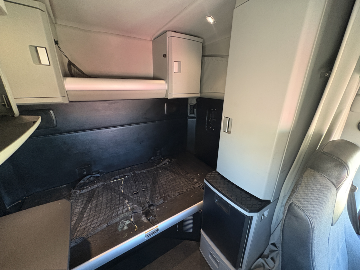 Kenworth T680 sleeper cab interior showing bunk area and storage cabinets, with mattress platform and overhead cabinets.