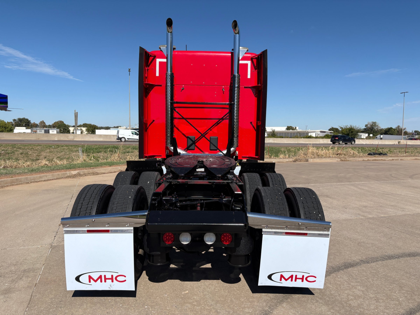 Rear view of a red Kenworth T680 tractor showing the chassis, dual rear axles, and white mud flaps labeled MHC.