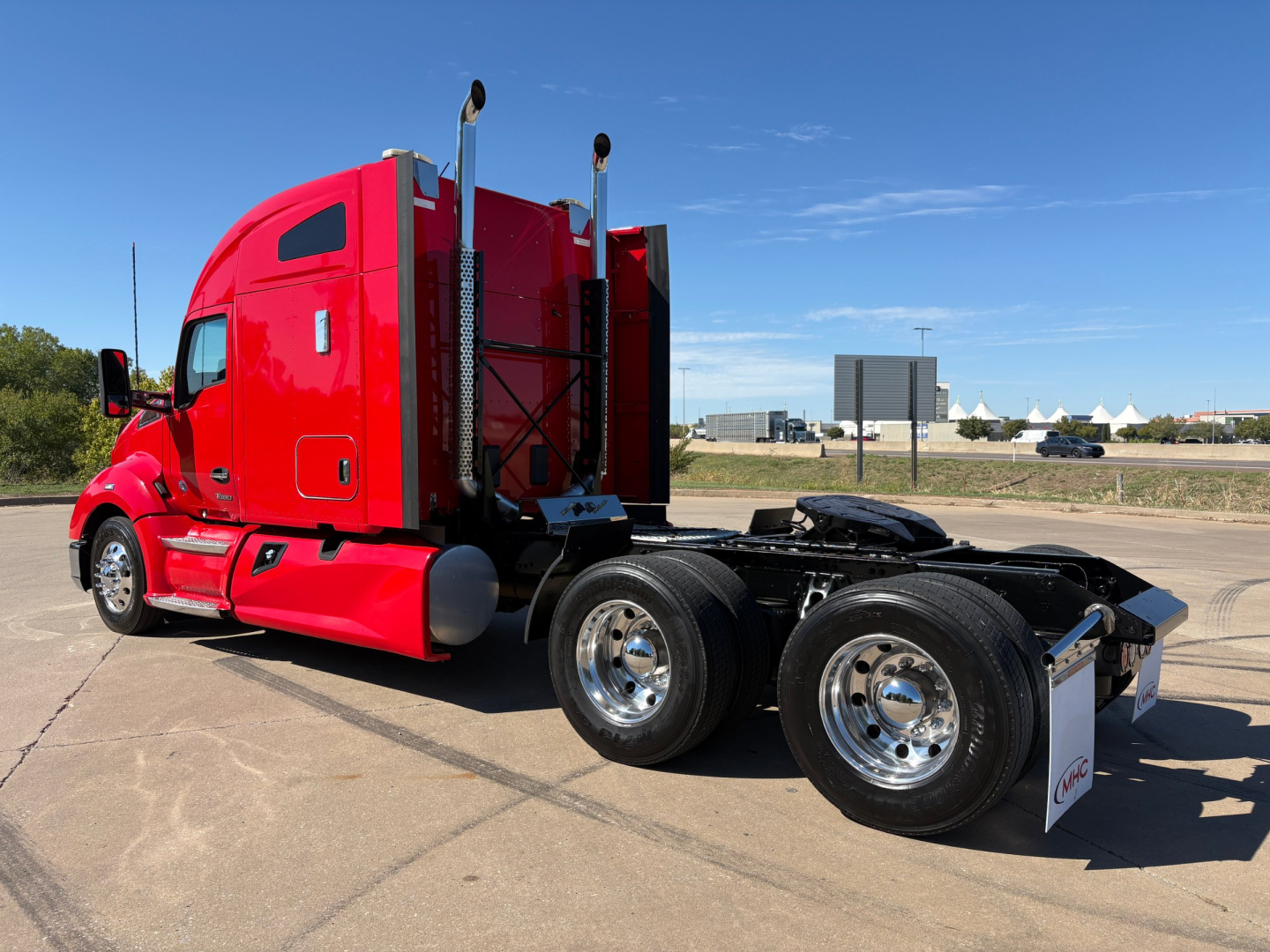 Kenworth T680 tractor sleeper cab side view showing dual rear wheels and red glossy paint with chrome fuel tanks and exhaust stacks.