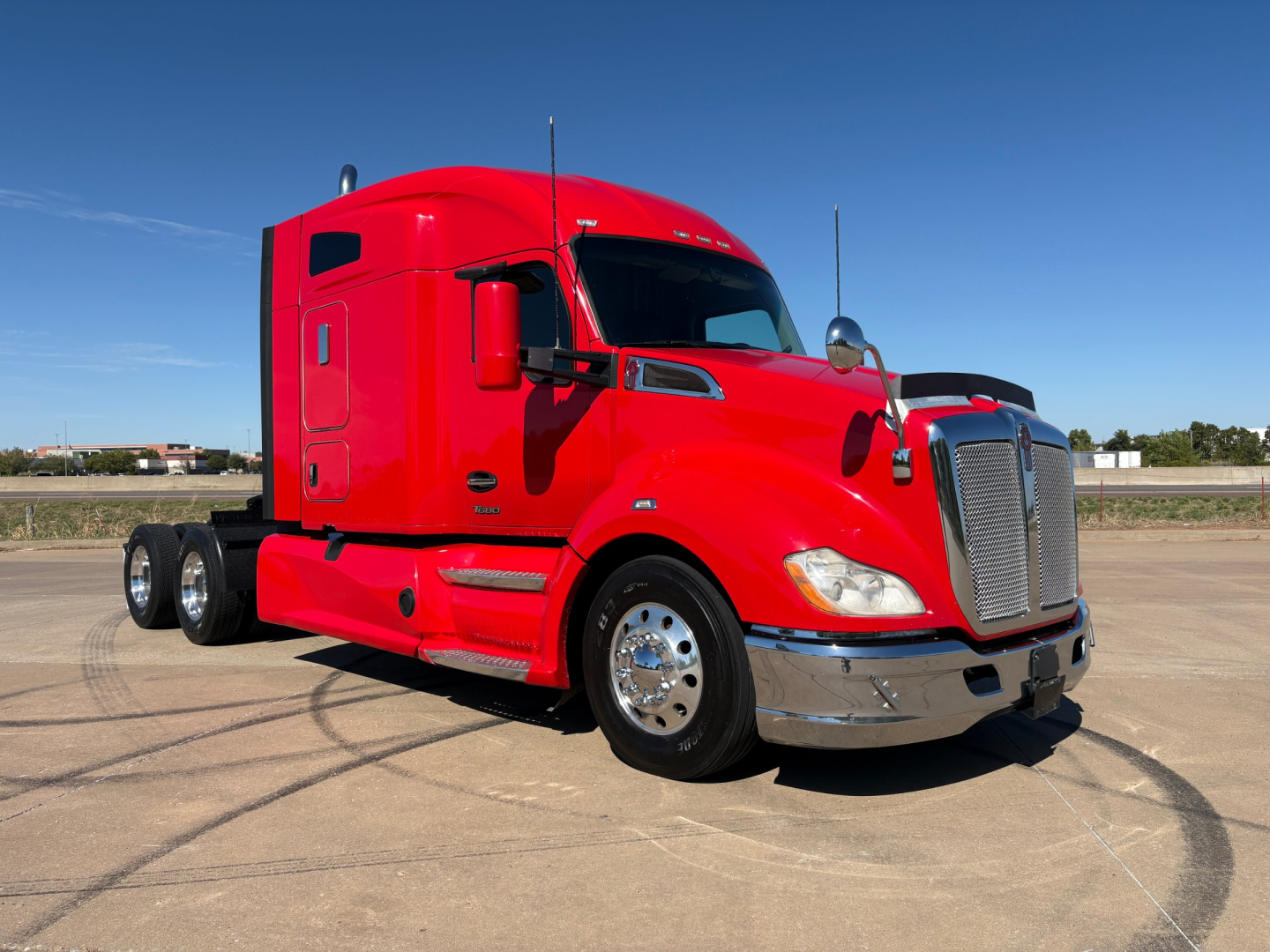 Kenworth T680 truck in red color, front three-quarter view, side mirrors, hood, and chrome bumper visible.