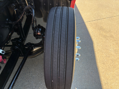 Kenworth T680 front wheel and suspension view showing tire and part of chassis and air lines.