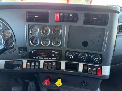 Kenworth T680 interior dashboard showing instrument cluster, climate controls, and switches; red emergency/hazard button, air vents, no stereo visible; multiple gauges with chrome bezels.