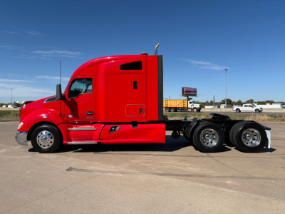 Side view of a red Kenworth tractor truck with sleeper cab and three rear wheels visible.