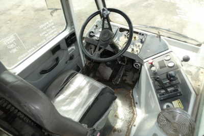 Kalmar Ottawa YT50 operator cockpit with steering wheel, dashboard, and seat; worn interior, exposed pedals and control levers.