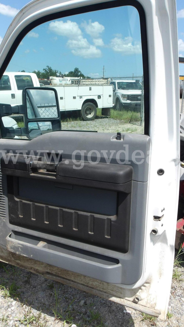 Ford F-250 truck door panel and window with side mirror visible; reflection shows utility trucks in a lot.