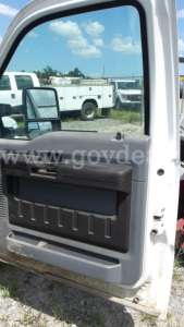 Ford F-250 truck door panel and window with side mirror visible; reflection shows utility trucks in a lot.