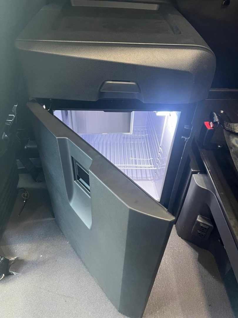 Cabin area showing a compact refrigerator with door open in a Freightliner Cascadia sleeper cab, with interior components nearby.