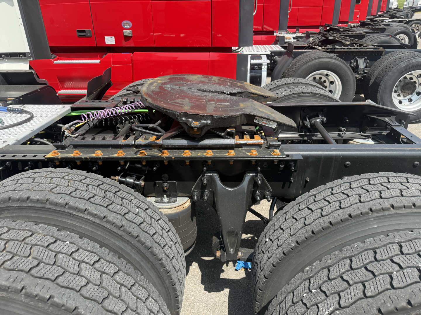 Red International LT625 truck cab in background with fifth wheel and dual rear axles; focus on chassis and hub area showing spare wheel, wiring, and frame components.
