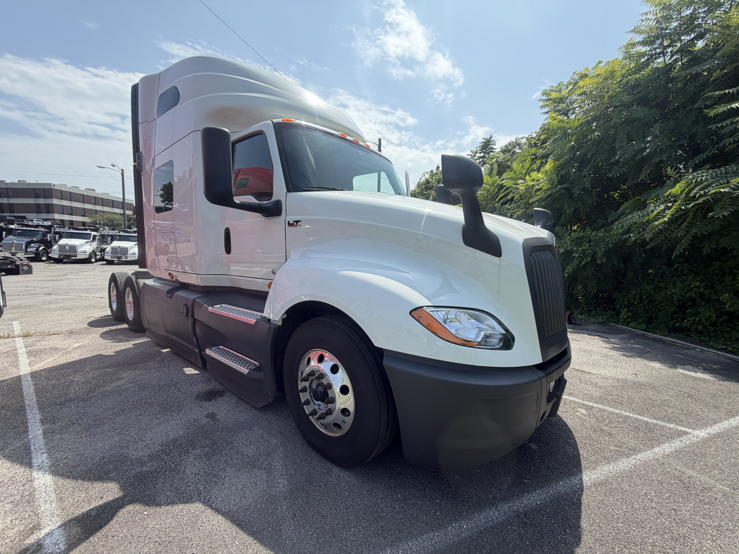 Truck cab in view showing white International LT625 sleeper tractor with large black bumper, side mirrors, and dual rear axles.