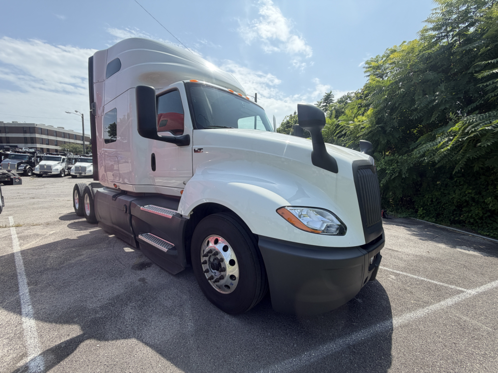 Truck cab in view showing white International LT625 sleeper tractor with large black bumper, side mirrors, and dual rear axles.