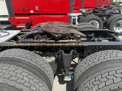 Red International LT625 truck cab in background with fifth wheel and dual rear axles; focus on chassis and hub area showing spare wheel, wiring, and frame components.