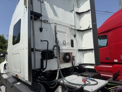 Truck sleeper cab rear view showing vertical aerodynamic fairing, OEM cooling unit and attached hoses; white exterior with ladder area and black steps.