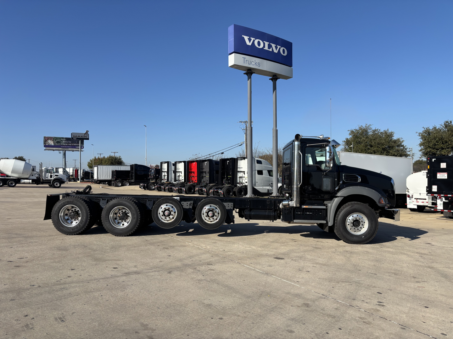 2025 Mack GR64B cab and chassis truck side view showing multiple axles and Volvo Trucks sign in lot.