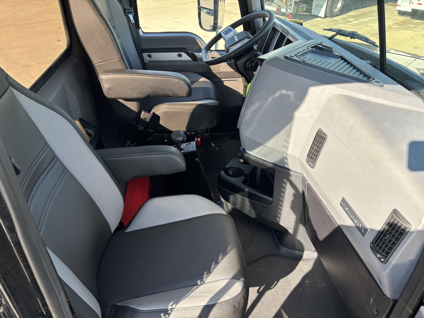 Cab and chassis interior of 2025 Mack GR64B showing driver seat and steering wheel, dashboard, and front passenger seat with gray upholstery.