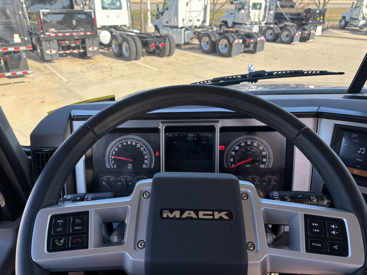 Mack GR64B cabin and steering wheel view showing dashboard gauges and center console with Mack logo.