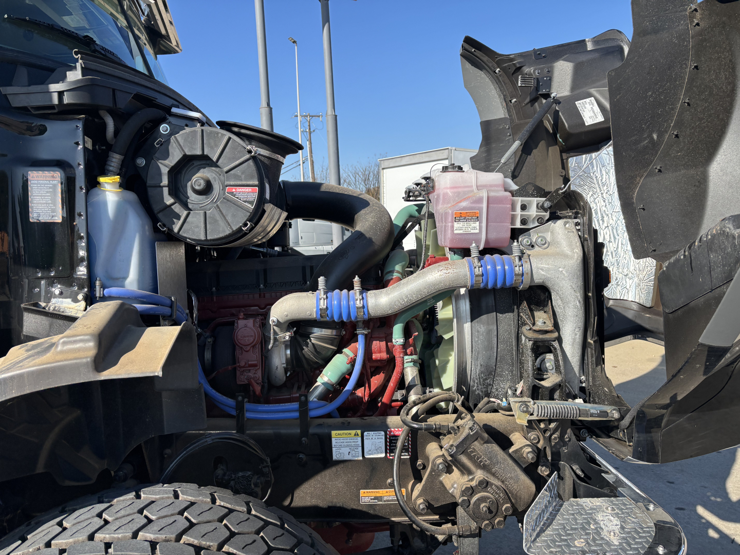 Engine bay of a new 2025 Mack GR64B cab and chassis showing coolant reservoir, hoses, and turbo/intercooler components.