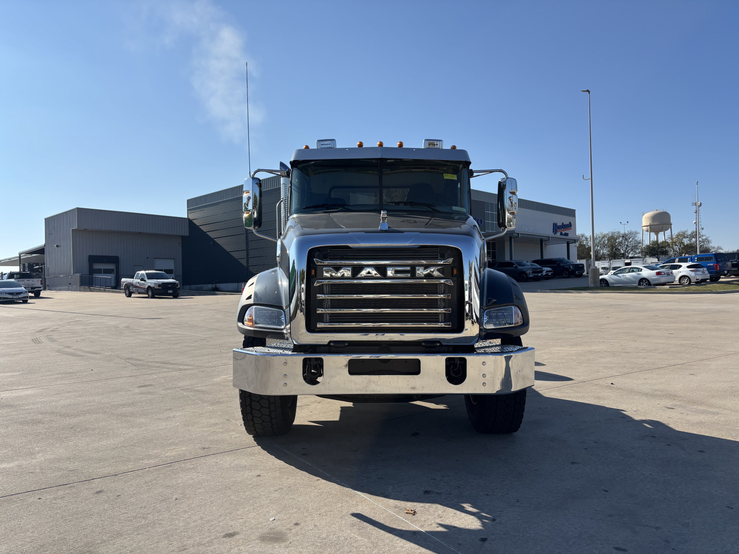 Front view of a 2025 Mack GR64B cab and chassis showing prominent grille with 'MACK' lettering, chrome bumper, dual headlights, and cargo area behind cab.